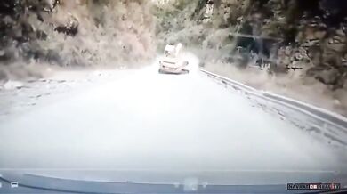 Bagr řítící se proti couvajícímu autu na horské silnici