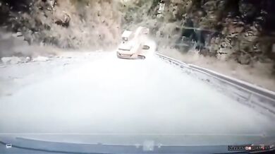 Bagr řítící se proti couvajícímu autu na horské silnici