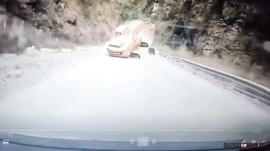 Bagr řítící se proti couvajícímu autu na horské silnici